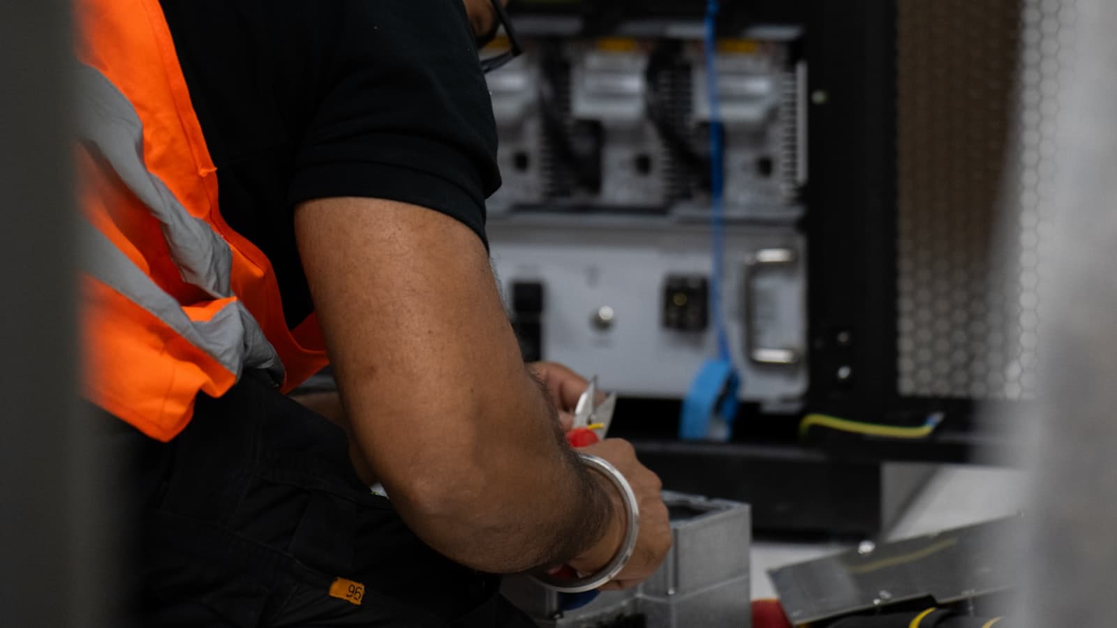 A technician in a high visibility vest working at an open server rack